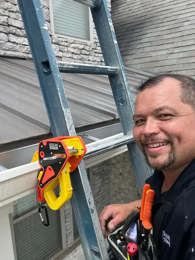 Smiling handyman on a ladder at a gutter with a tool pouch on his belt