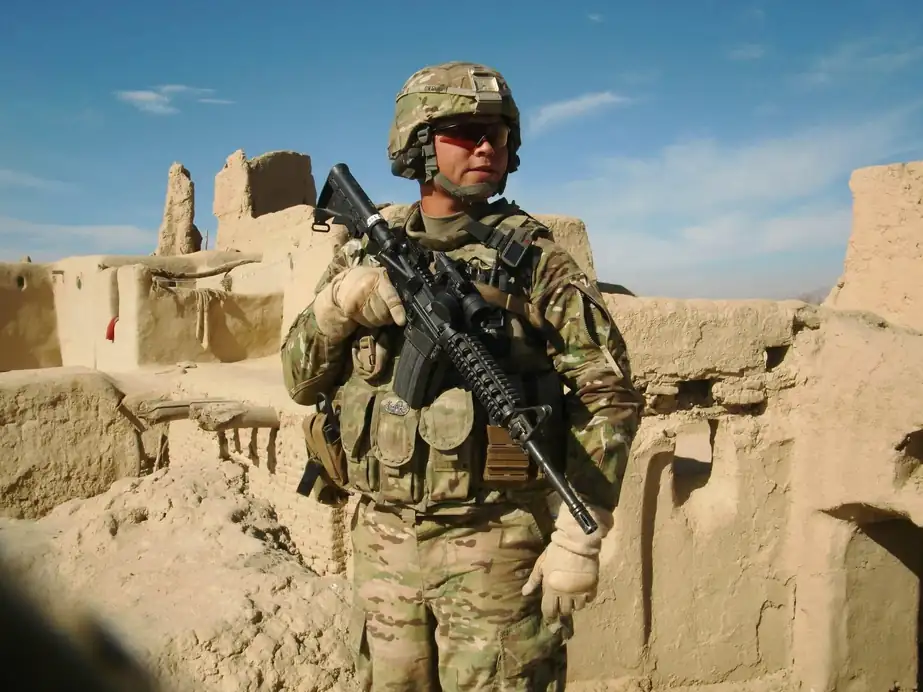 Robbie during his military service, standing in full field kit against mud-brick walls in a desert setting