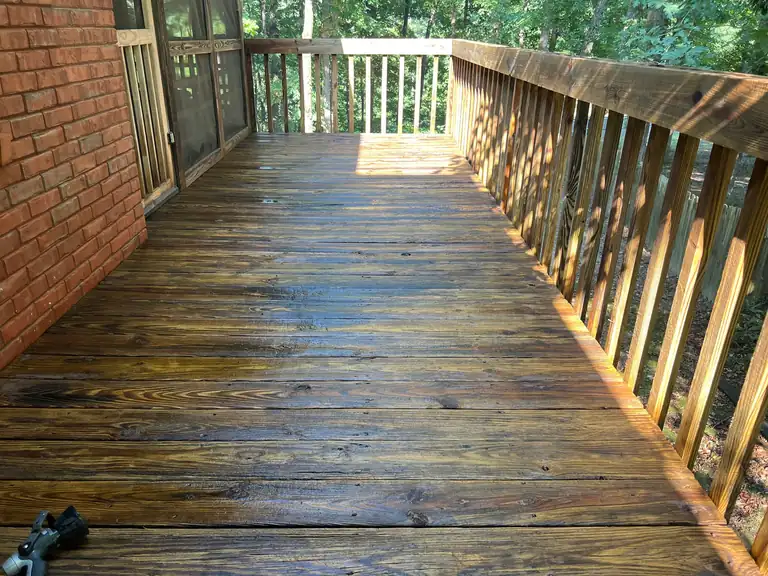 Wood deck with railings beside a brick wall, boards freshly cleaned