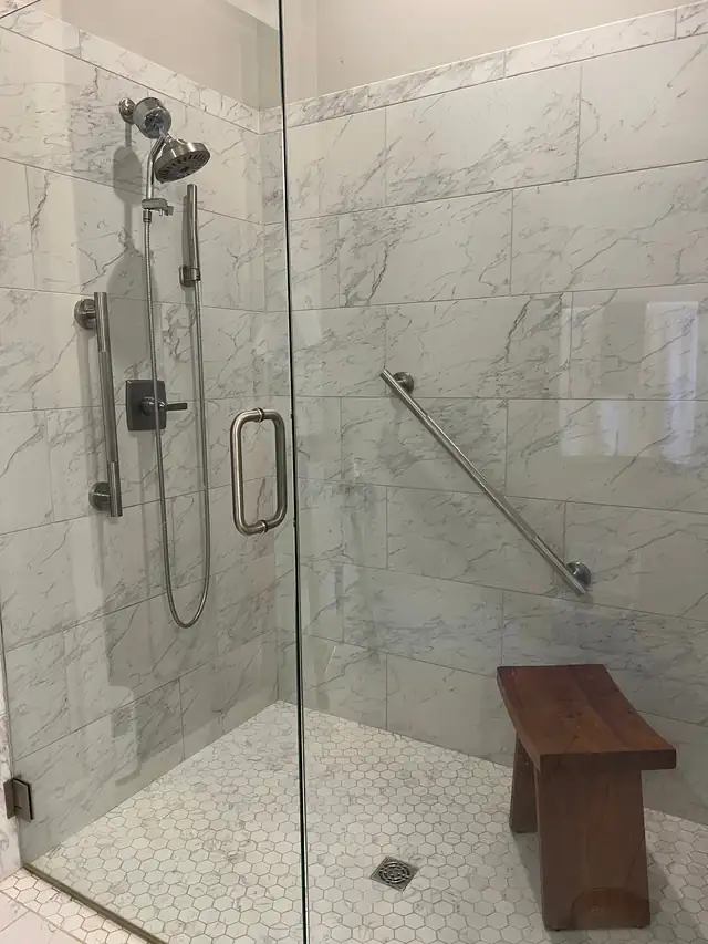 Walk-in tiled shower with two stainless grab bars and a wooden bench