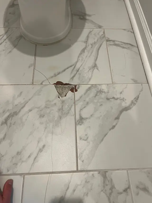 Cracked marble-look floor tile beside the base of a toilet